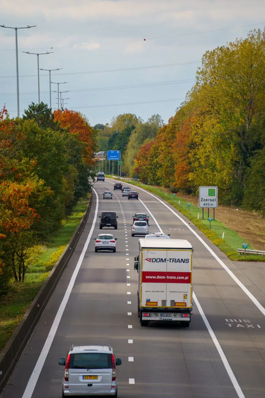 Ruch na autostradzie jesienią, kolorowe liście wzdłuż drogi mienią się żywymi barwami jesieni.