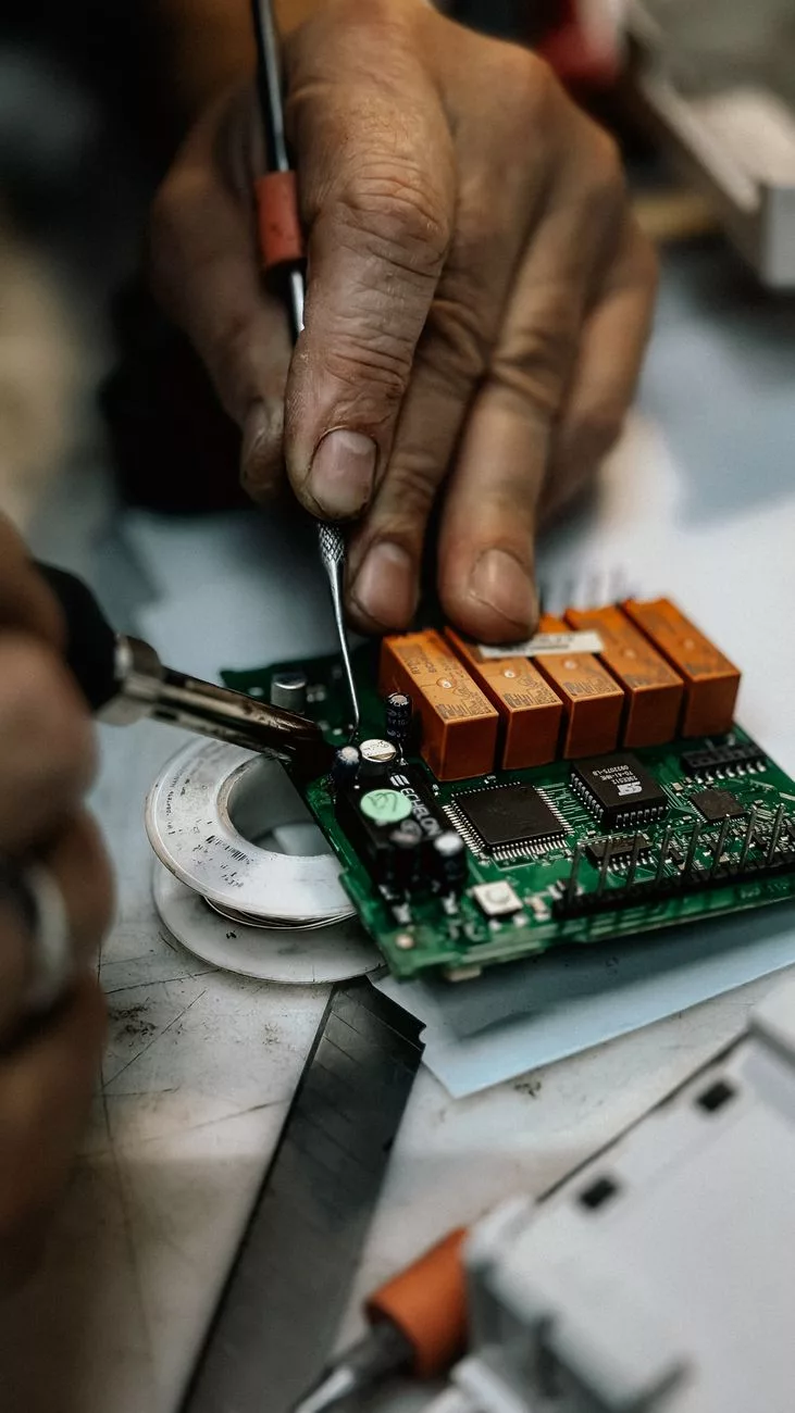 Szczegółowy obraz rąk lutujących i naprawiających płytkę elektroniczną.
