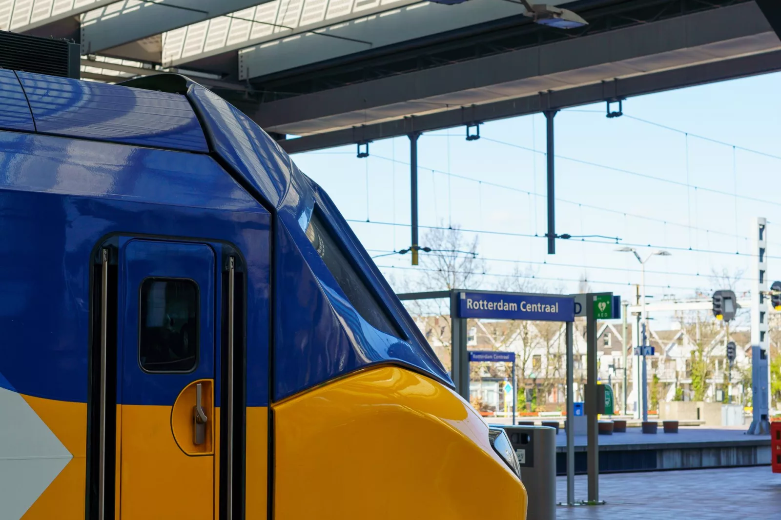 Kolorowy holenderski pociąg na dworcu kolejowym Rotterdam Centraal w pogodny dzień, prezentujący nowoczesny transport publiczny.