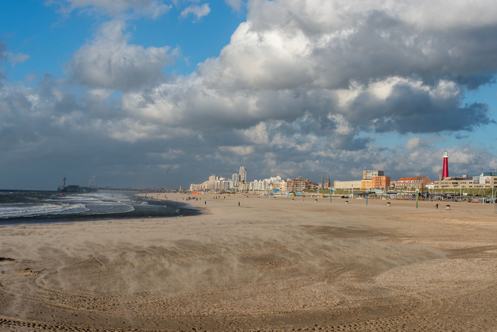 Tętniąca życiem letnia panorama plaży Scheveningen z diabelskim młynem i czerwoną latarnią morską w Hadze, w Holandii.